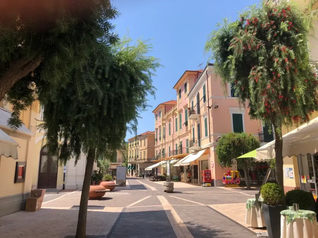 Via pedonale del centro storico di Diano Marina con palazzi color pastello, negozi e alberi fioriti, Riviera Ligure